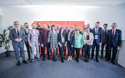 grupa kobiet i mężczyzn w średnim wieku stojąca  na tle ścianki z logo jubileuszu Politechniki łódzkiej