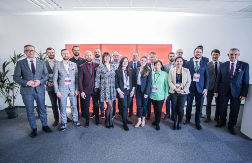 grupa kobiet i mężczyzn w średnim wieku stojąca  na tle ścianki z logo jubileuszu Politechniki łódzkiej