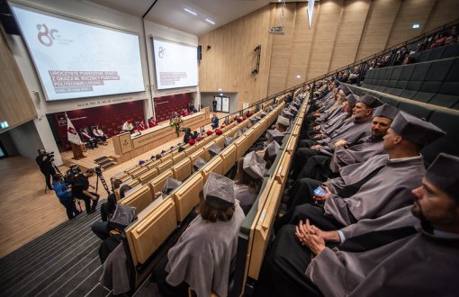 członkowie senatu ubrani w tradycyjne togi koloru szarego, przed nimi telebim z wyświetlonym slajdem z okazji 80-lecia politechniki Łódzkiej